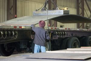 worker loading large metal section onto flatbed trailer